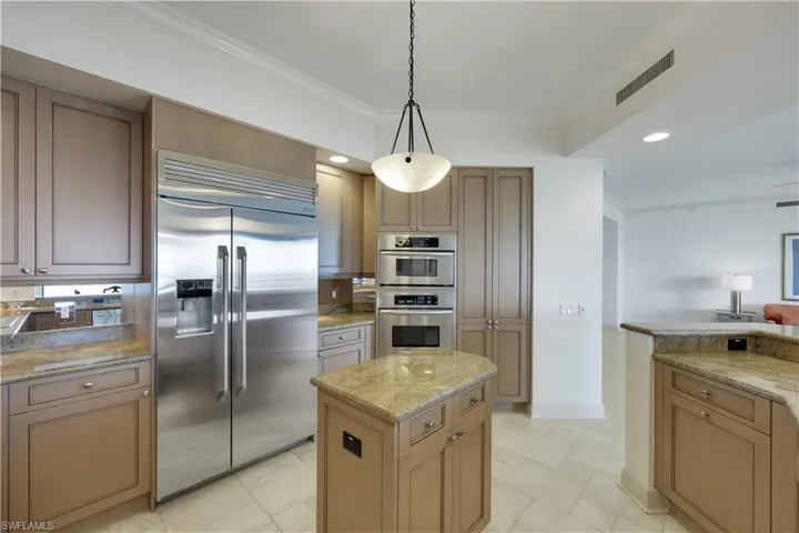 Kitchen featuring light stone counters, decorative light fixtures, ornamental molding, and stainless steel appliances