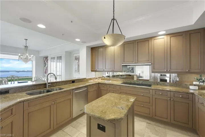 Kitchen with sink, ornamental molding, appliances with stainless steel finishes, pendant lighting, and light stone countertops