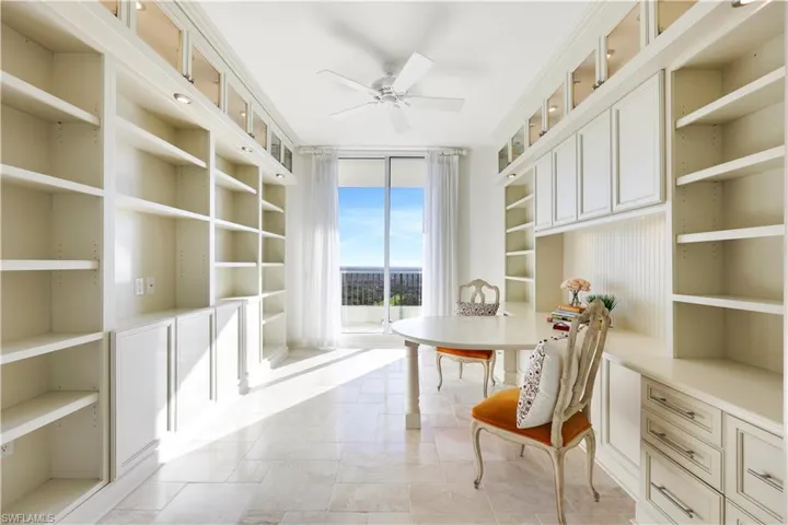 Home office with built in shelves, ceiling fan, and a wall of windows