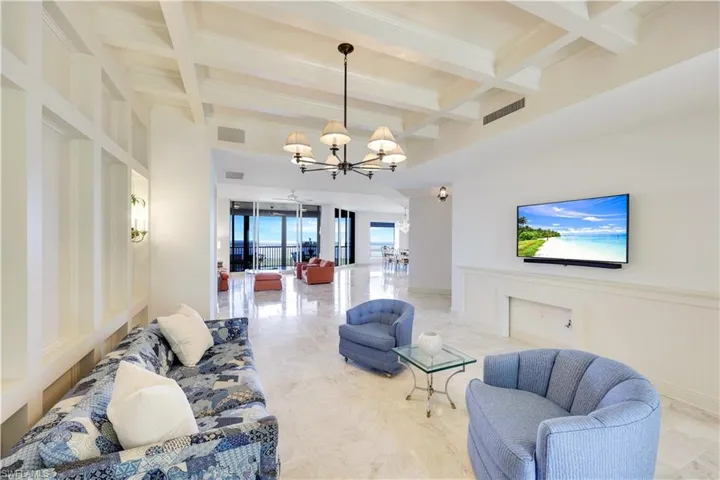 Living room featuring beamed ceiling, coffered ceiling, and a chandelier
