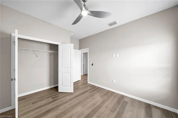 Unfurnished bedroom featuring lofted ceiling, a closet, visible vents, wood finished floors, and baseboards