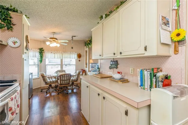 Kitchen featuring wallpapered walls, light countertops, dark wood-type flooring, cream cabinets, and a textured ceiling