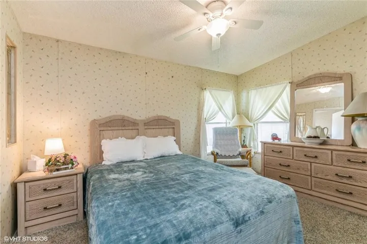 Bedroom featuring a textured ceiling, carpet flooring, ceiling fan, and wallpapered walls