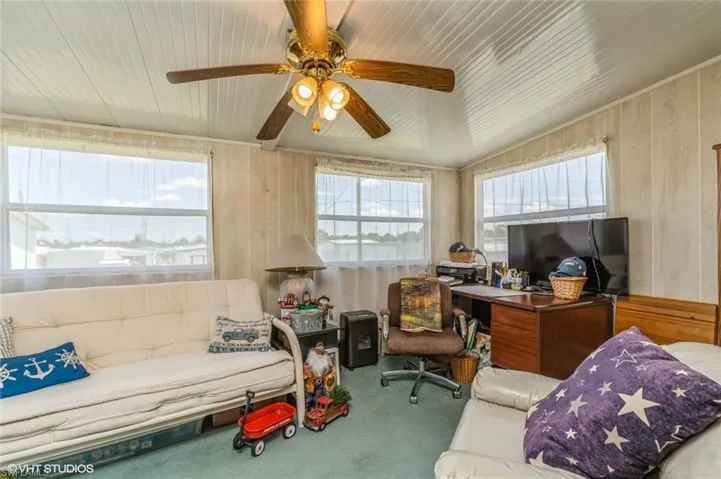 Carpeted office featuring wood walls and a ceiling fan