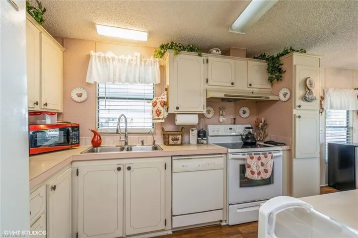 Kitchen featuring white appliances, light countertops, a textured ceiling, under cabinet range hood, and wallpapered walls