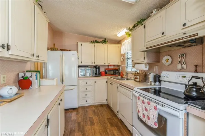 Kitchen featuring white appliances, light countertops, a textured ceiling, dark wood-style flooring, and under cabinet range hood