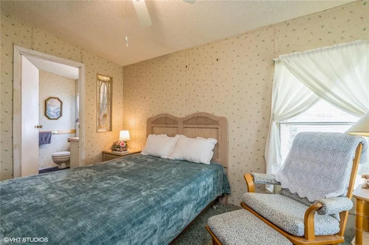 Bedroom featuring a textured ceiling, connected bathroom, ceiling fan, wallpapered walls, and carpet flooring
