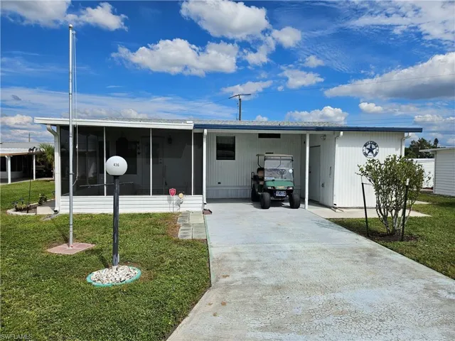 Manufactured / mobile home featuring a front lawn, concrete driveway, a sunroom, and a carport