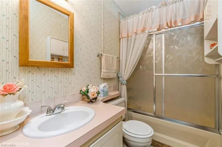 Full bathroom with shower / bath combination with glass door, wallpapered walls, and vanity