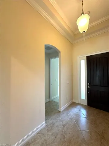 Foyer with arched walkways, light tile patterned flooring, crown molding, and a tray ceiling