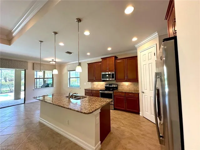 Kitchen featuring ornamental molding, stainless steel appliances, pendant lighting, decorative backsplash, and dark stone counters
