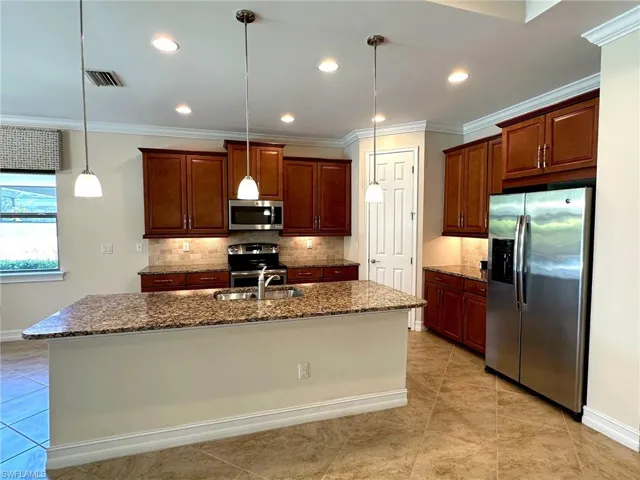 Kitchen featuring dark stone countertops, stainless steel appliances, backsplash, crown molding, and pendant lighting