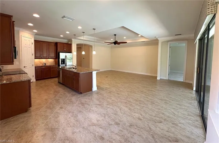 Kitchen featuring hanging light fixtures, a raised ceiling, dark stone countertops, crown molding, and a ceiling fan