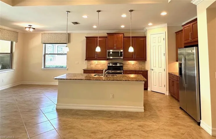 Kitchen featuring appliances with stainless steel finishes, backsplash, dark stone counters, pendant lighting, and ornamental molding