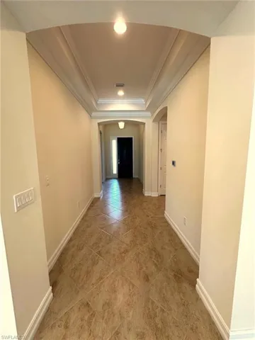 Hall featuring arched walkways, a tray ceiling, crown molding, and light tile patterned floors