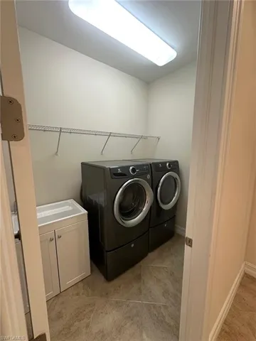 Laundry area with tiled floors, upgraded washer and clothes dryer, and sink with cabinet space.