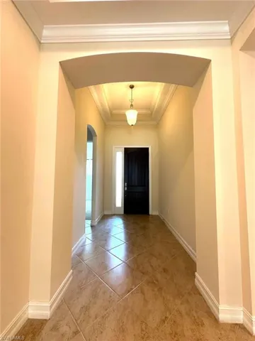 Foyer with arched walkways, ornamental molding, light tile patterned floors, and a tray ceiling