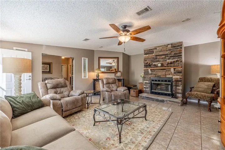 Living area featuring light tile patterned floors, visible vents, ceiling fan, a stone fireplace, and a textured ceiling