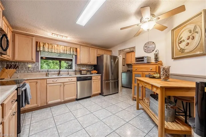 Kitchen featuring light tile patterned floors, light countertops, decorative backsplash, appliances with stainless steel finishes, and a sink