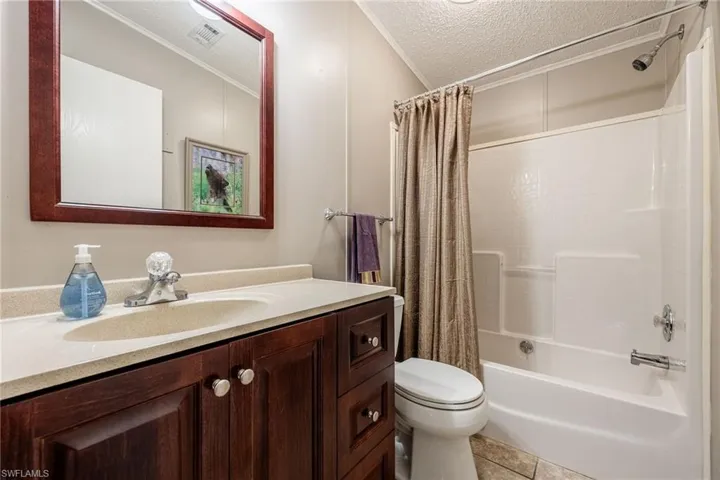 Full bathroom featuring a textured ceiling, toilet, vanity, visible vents, and tile patterned floors