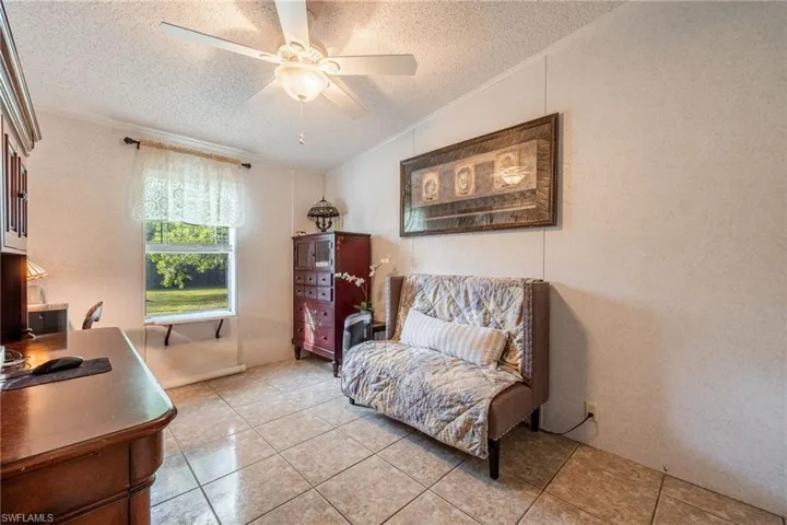 Living area with a textured ceiling, ceiling fan, light tile patterned floors, vaulted ceiling, and crown molding