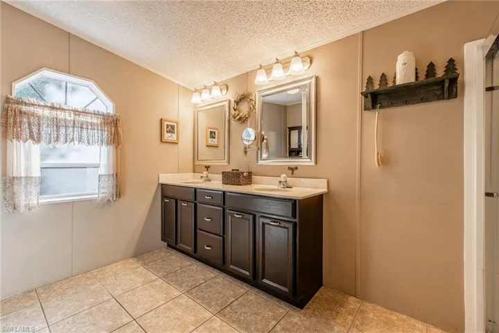 Bathroom with tile patterned flooring, a sink, a textured ceiling, and double vanity