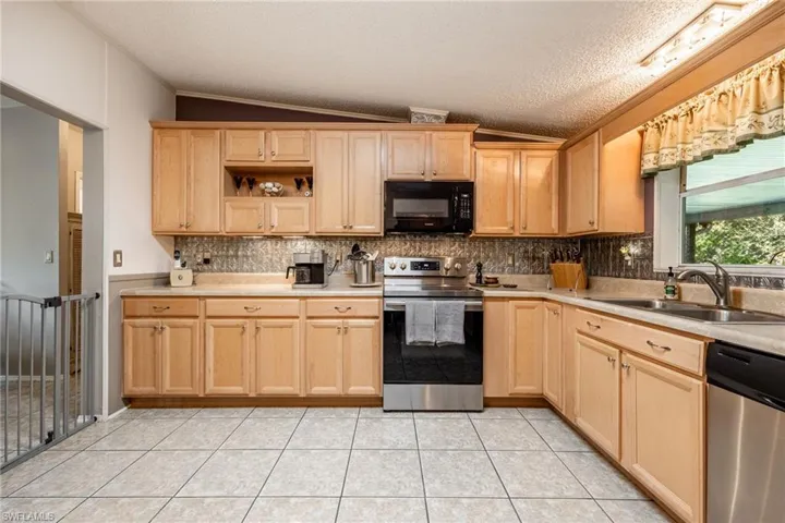 Kitchen with light tile patterned floors, light brown cabinets, a sink, vaulted ceiling, and appliances with stainless steel finishes