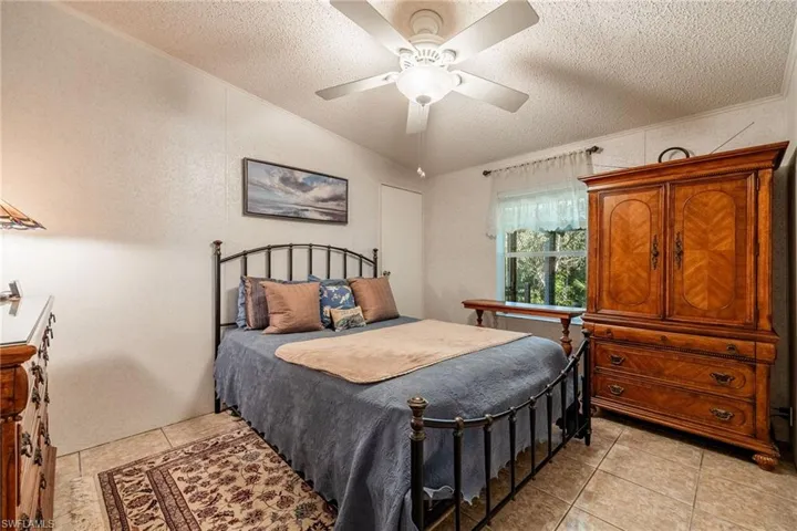 Bedroom with a ceiling fan, light tile patterned flooring, crown molding, and a textured ceiling