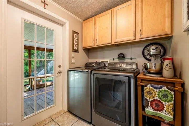Laundry room with light tile patterned floors, cabinet space, ornamental molding, a textured ceiling, and independent washer and dryer