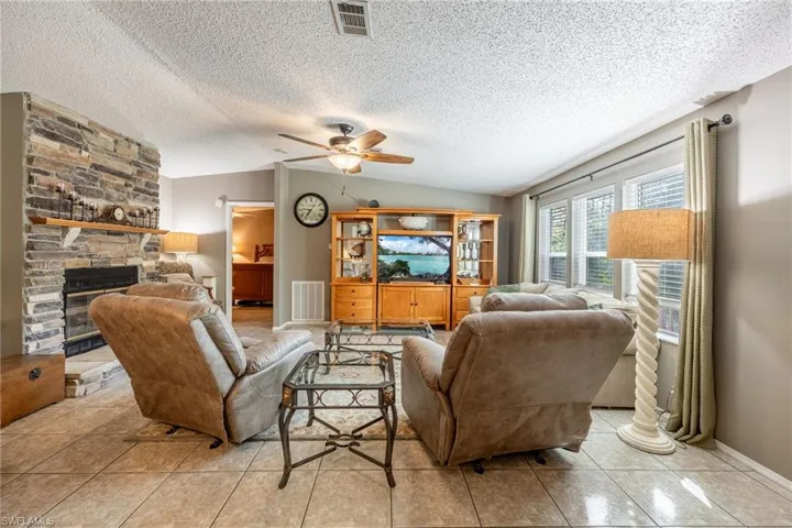 Living room with lofted ceiling, a fireplace, visible vents, and a ceiling fan