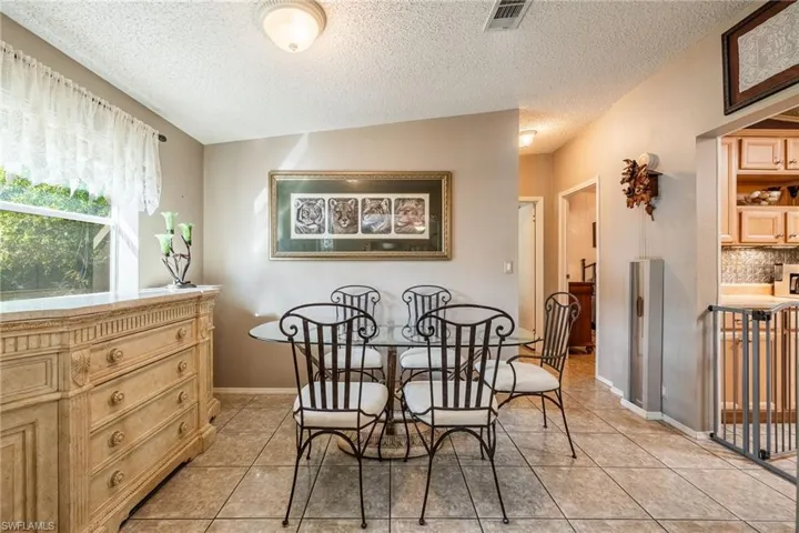 Dining area with a textured ceiling, light tile patterned flooring, visible vents, and baseboards
