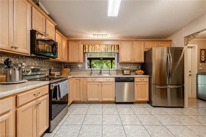 Kitchen featuring stainless steel appliances, light countertops, backsplash, light tile patterned flooring, and a sink