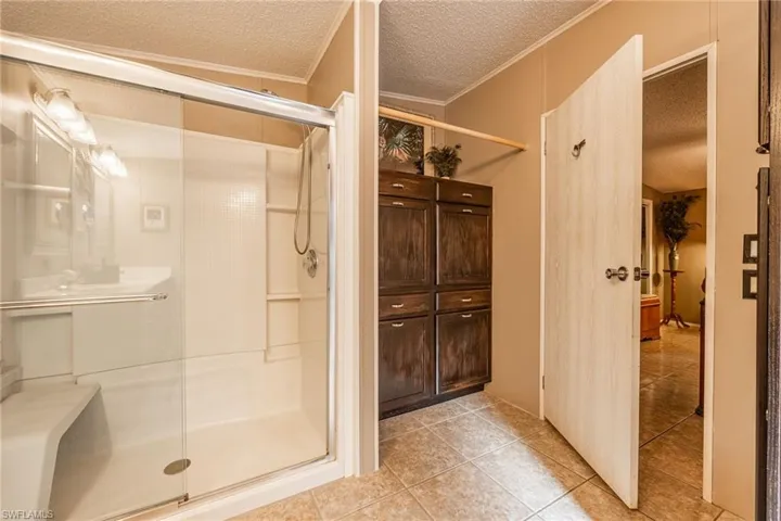 Full bathroom featuring tile patterned flooring, crown molding, a shower stall, and a textured ceiling