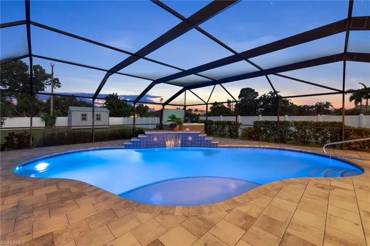 Pool at dusk with glass enclosure, a patio area, and pool water feature