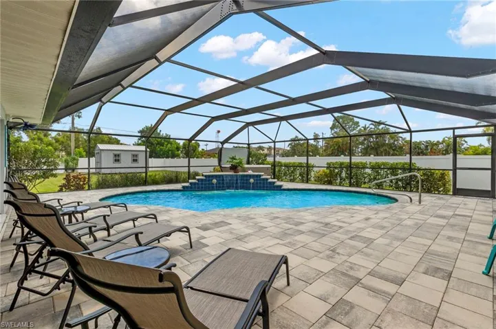 View of pool featuring a patio area, pool water feature, an outdoor structure, and a lanai