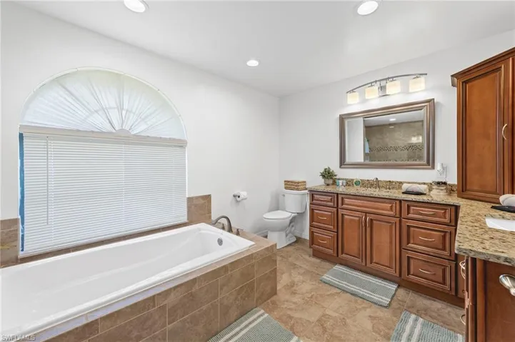 Bathroom featuring tile flooring, tiled bath, vanity, and toilet