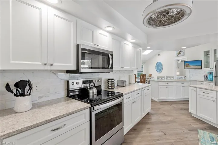 Kitchen with appliances with stainless steel finishes, white cabinetry, light hardwood / wood-style flooring, and tasteful backsplash