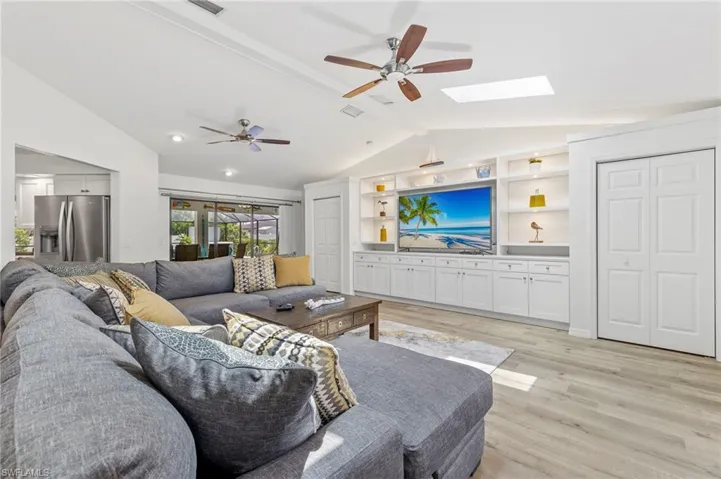 Living room with ceiling fan, light hardwood / wood-style flooring, built in shelves, and lofted ceiling with skylight
