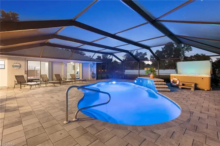 Pool at dusk featuring glass enclosure, a hot tub, and a patio