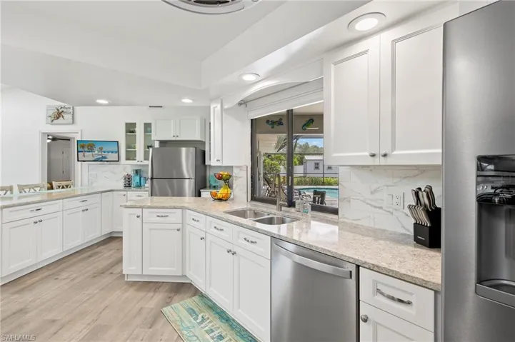 Kitchen with light hardwood / wood-style floors, stainless steel appliances, white cabinets, sink, and tasteful backsplash