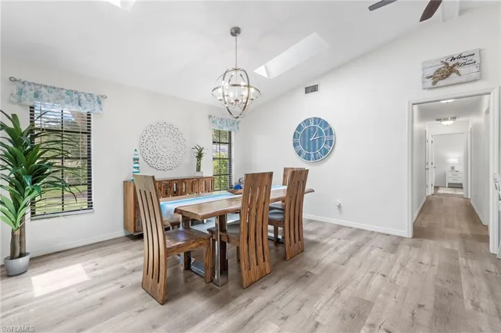 Dining space featuring vaulted ceiling with skylight, light hardwood / wood-style floors, and ceiling fan with notable chandelier