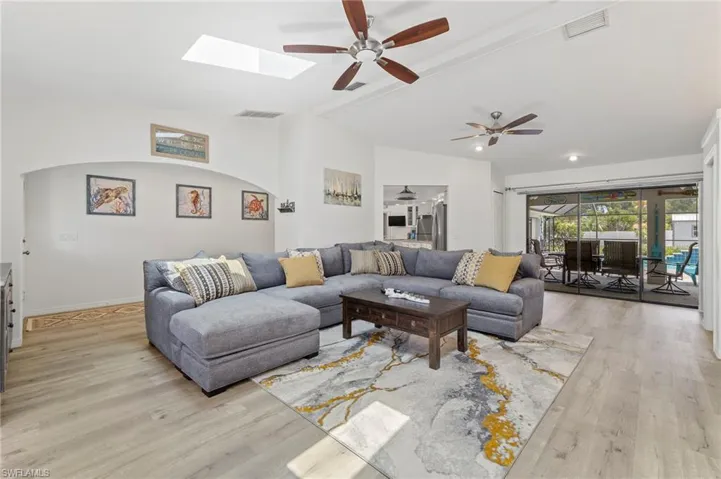 Living room with ceiling fan, light hardwood / wood-style floors, and lofted ceiling with skylight