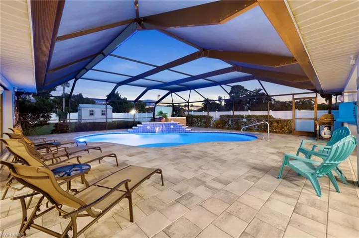 Pool at dusk featuring a patio area, pool water feature, a lanai, and a storage shed