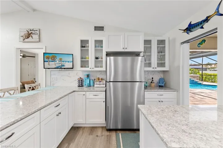 Kitchen with lofted ceiling with beams, light hardwood / wood-style flooring, stainless steel refrigerator, tasteful backsplash, and ceiling fan