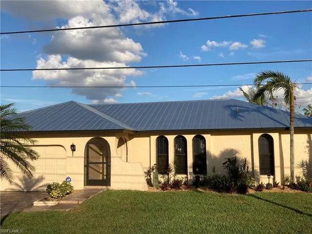 View of front of house with stucco siding, a garage, a front lawn, a metal roof, and driveway