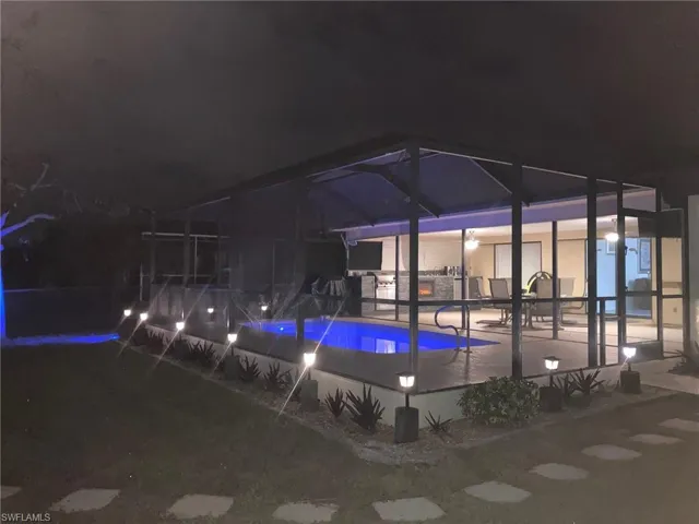 Pool at night featuring an outdoor pool, a sunroom, and glass enclosure