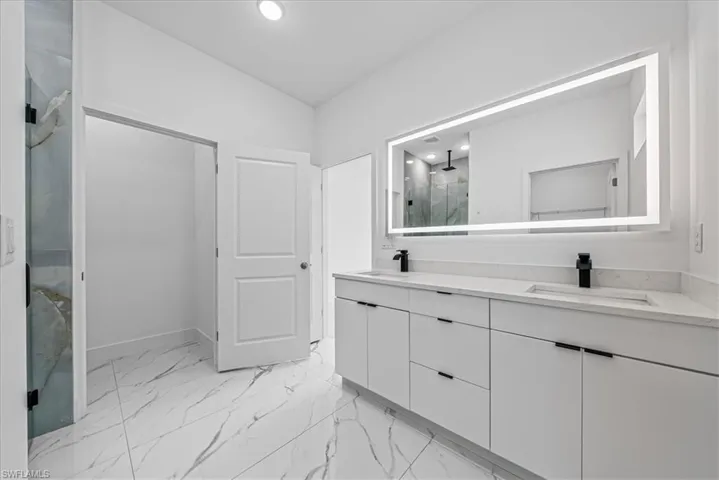 Bathroom with double vanity, a marble finish shower, light marble finish flooring, and recessed lighting