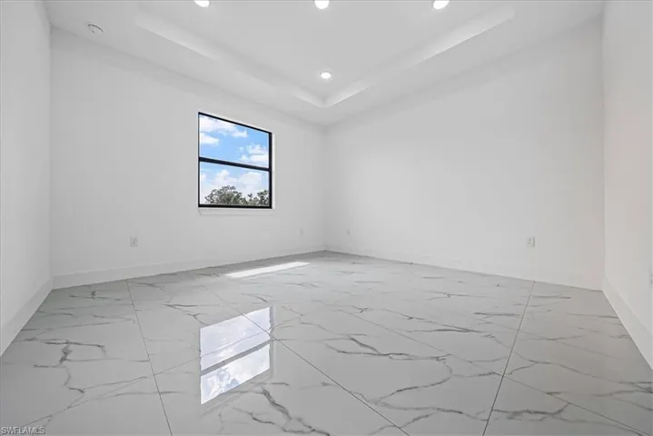 Empty room featuring light marble finish flooring, recessed lighting, and a raised ceiling