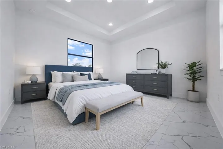 Bedroom with a raised ceiling, recessed lighting, and light marble finish floors