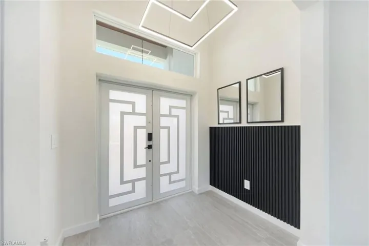 Entryway featuring double doors with geometric glass inserts, transom window, contemporary ceiling light fixture, accent wall with vertical paneling, and large format tile flooring